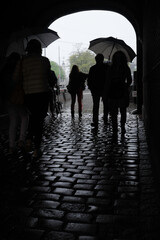 Unrecognizable people shelter from the rain with umbrellas in a stone archway at the Binnenhof in the city of The Hague, the Netherlands