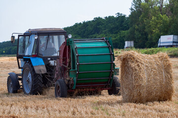 tractor makes big straw roll on yellow field at summer day