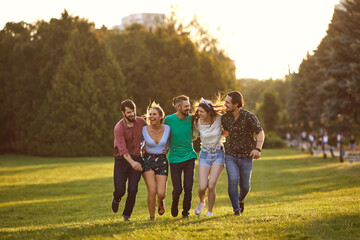 A group of young people are having fun hugging along the grass in a summer park.
