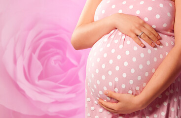 pregnant woman holding her belly over pink rose backdrop