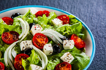 Fresh Greek salad - feta cheese, cherry tomatoes, lettuce, black olives and onion on black stone board
