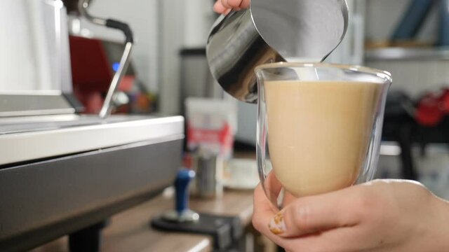 Coffee making proccess. Barista cooking coffee and pours thick and fresh hot milk into transparent mug. Close-up shot of barista pouring milk To make Latte. Slow motion. Full hd