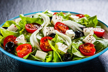 Fresh Greek salad - feta cheese, cherry tomatoes, lettuce, black olives and onion on black stone board
