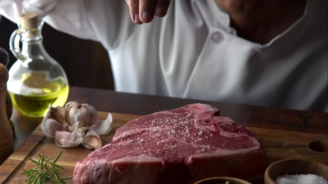 chef seasoning t-bone steak with salt 
