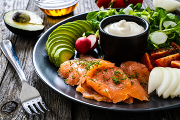 Breakfast - smoked salmon, avocado, garlic creamy dip and vegetable salad on wooden table
