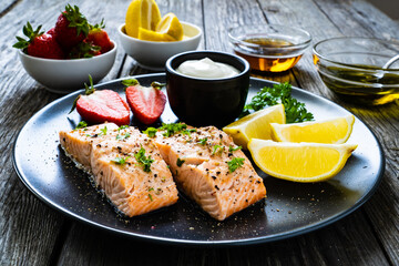 Steamed salmon steaks with lemon, strawberries and creamy dip served on black plate on wooden table
