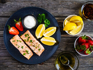 Steamed salmon steaks with lemon, strawberries and creamy dip served on black plate on wooden table
