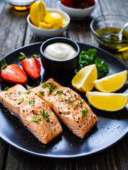 Steamed salmon steaks with lemon, strawberries and creamy dip served on black plate on wooden table

