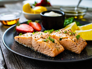 Steamed salmon steaks with lemon, strawberries and creamy dip served on black plate on wooden table
