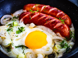 Fried sausages with egg and onion in frying pan