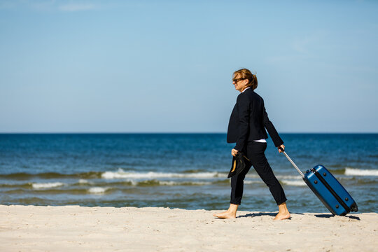 Businesswoman walking with suitcase on beach
