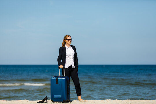 Businesswoman walking with suitcase on beach

