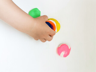 Toddler sculpts from colored plasticine on a white table. The hand of a small child squeezes pieces of colored plasticine. Children's creativity, educational games, fine motor skills. Top view. 