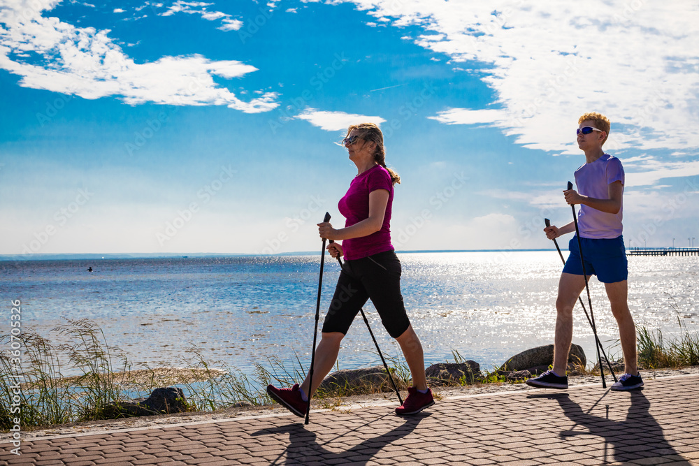 Wall mural Nordic walking - middle-aged woman and young man training by the sea shore