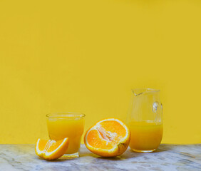 fresh orange juice in glass and decanter and sliced fresh oranges. Yellow background. Summer concept