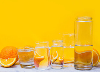 Oranges distorted through the glasses with water. Yellow background. Summer concept