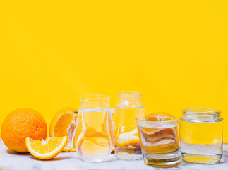 Oranges distorted through the glasses with water. Yellow background. Summer concept