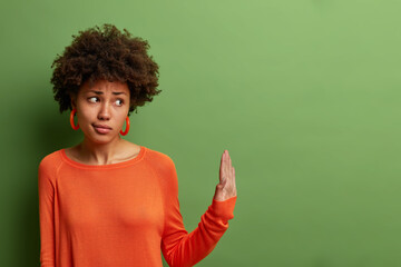 Serious displeased dark skinned woman shows palms sideways in prohibition gesture, refuses...