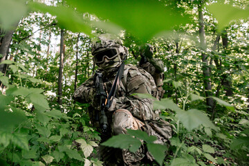 Two soldiers with weapons in the forest thicket sitting among the green leaves