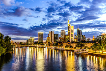 Frankfurt am Main. European finance center city downtown skyline cityscape. Eiserner steg bridge, river during twilight blue hour, sunset, evening, night. Gold yellow color. Travel in Hesse, Germany.