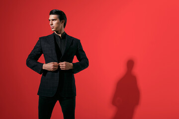 Obraz na płótnie Canvas Horizontal view. Young handsome brunette man in black elegant suit over red background. Copy space.