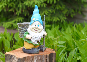 Garden figures. The figure of a dwarf in the garden. The gnome stands on the stump on a green background. Cute dwarf against the green grass. Garden sculpture