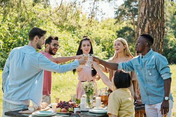 Group of happy multi-ethnic friends toasting over table served for dinner
