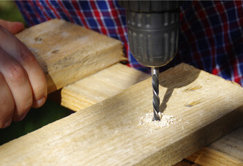A carpenter with a drill in hand makes a hole in the wooden board