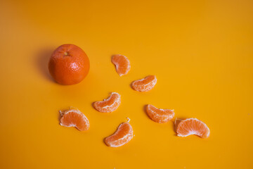 One whole tangerine with lots of slices on an orange background. Concept photo. Top view.