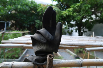 The right hand of black gardening glove which was hung on bamboo stick  showed the fingers as a sign  language.