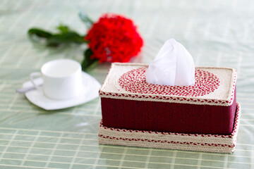 Deep red Handmade fiber Napkin box on the dining table with a red flower and a white tea-cup. Tissue paper box on restaurant.