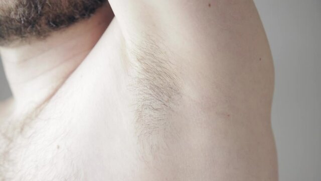 Close up slow motion shoot of man touching his hairy armpit before procedure of depilation or shaving. Removal of unwanted hair on body parts in cosmetology. Using of deodorant or antiperspirant