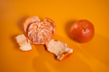 Whole tangerine with wedges on an orange background. Concept photo. With copy space.
