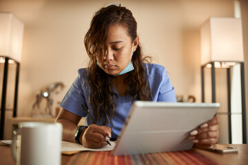 Fototapeta premium filipina nurse working from home doing paperwork and using tablet