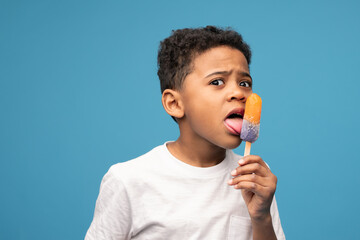 Little boy of African ethnicity licking ice cream with taste of juicy orange - obrazy, fototapety, plakaty