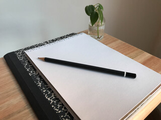 Pencil with a sketchbook on a woden table and a small plant