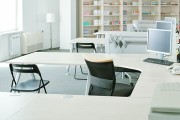 Row of desks with computer monitors and chairs near by on background of shelves