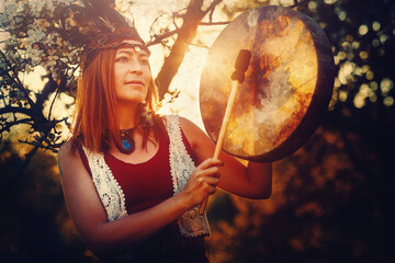 beautiful shamanic girl playing on shaman frame drum in the nature.