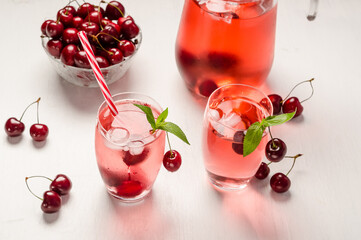 Summer cooling drink with cherries, ice and mint on a white wooden background.