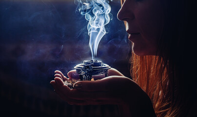 incense in a woman hand, incense smoke on a black background. - obrazy, fototapety, plakaty