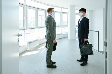 Two young contemporary businessmen in elegant suits and protective masks