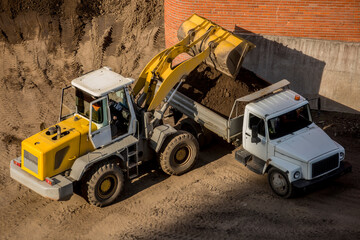 Yellow excavator loading dumper truck
