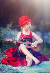 Little girl sitting on blanket and playing ukulele, Outdoor portrait.