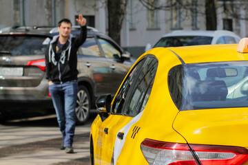 A yellow taxi pulls up to a young man in a black hoodie. The guy goes towards the car and waves to...