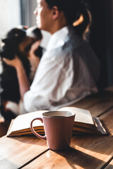 Yoman sitting in living room with her cute Bernese Mountain Dog dog, reading and drinking coffee.