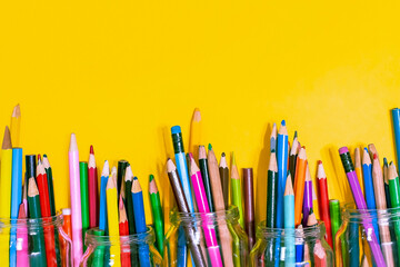 Many colored pencils are lying on the bottom of the bright yellow background. The place for the title is an empty sheet. Top view.
