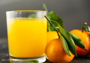 Fresh tangerine juice in a glass cup on a black background. Whole tangerines with green leaves lie nearby. Healthy eating concept