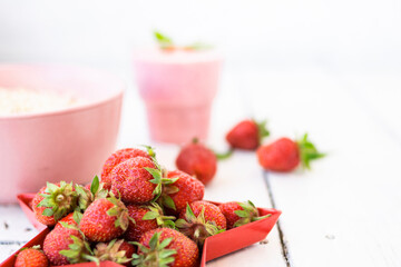 Fresh strawberry yogurt with berries around on a white wooden background. A pink shake in a glass, next to it is a pink cup with Hercules flakes, and red strawberries lie in a red star-shaped plate