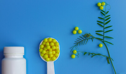 A measuring spoon filled with yellow dragees, a white bottle of medicine and a green sprig of a plant decorated with vitamins. Concept of plant food additives