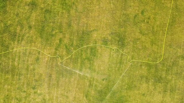 Top down aerial view of football field surface covered with green grass and sprinklers spraying water.